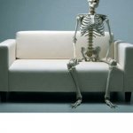 Still waiting skeleton sitting on sofa with legs apart