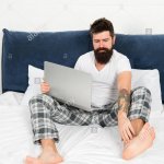 Guy in bed wearing pajamas with laptop