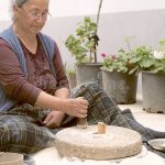 Woman using a hand-powered stone grist mill