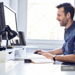 Smiling man working on computer at desk in office — casual, busi