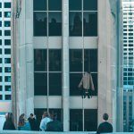 a man standing in a window on a very tall build with weird peopl