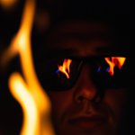 person staring into the fire in the dark with glasses on. flames
