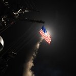 American ship launches cruise missile at night behind US flag