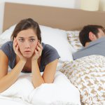 Anxious lady in bed next to sleeping man