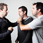 2 men fighting each other while guy looks at them