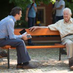 old man sitting on bench with stranger paying attention at him