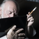 depressed old man smoking cigar at chromebook