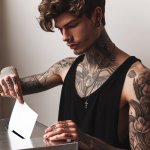 Young guy with tattoos and a nose ring puts ballot in ballot box