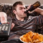 Man with beer and chips watching TV at home