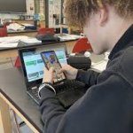 student hiding phone behind laptop