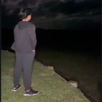 A boy standing by the riverside at night, lost in deep thoughts