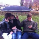 Guy on phone holding umbrella over kissing couple