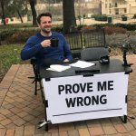 man sitting outside with a table and a sign that says prove me w