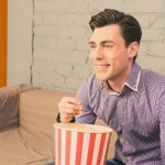 Guy with purple shirt & brown hair sitting & eating popcorn template