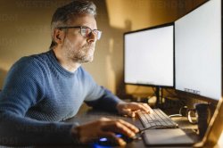 Mature man sitting at desk at home working on computer stock pho Meme Template