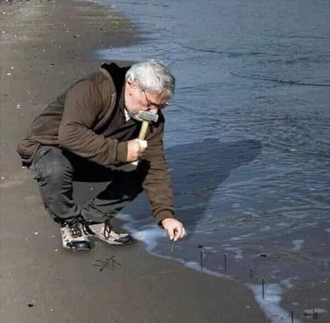Guy hammering nails into sand at the beach Blank Meme Template